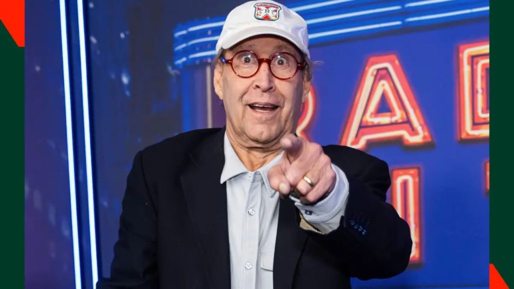 Actor Chevy Chase speaking on stage at a Christmas Vacation tour event with cheering fans.
