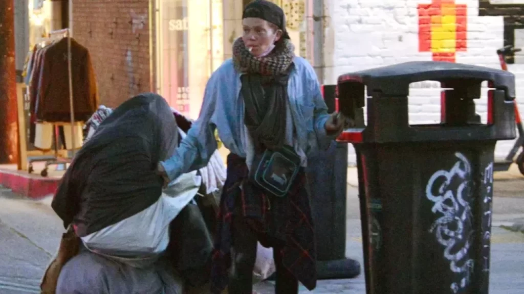 Loni Willison leaning by a dumpster or trash bin, rummaging for necessities in Los Angeles.
