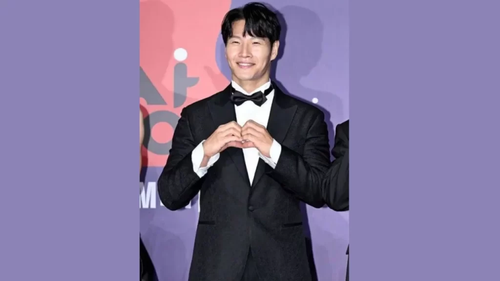Kim Jong Kook in a tuxedo making a playful gesture, showing his charm and personality.