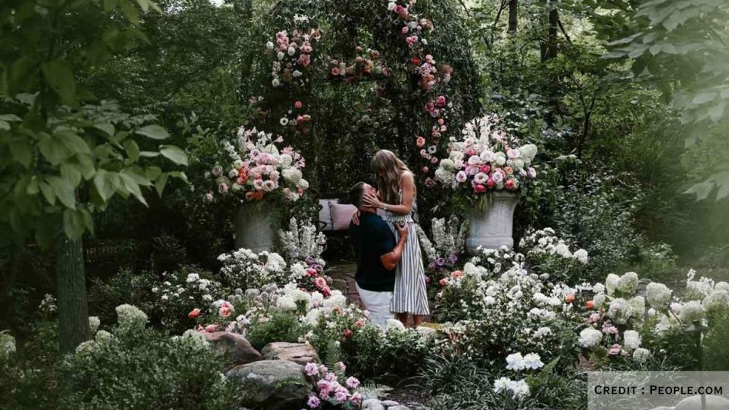 The couple poses in a garden filled with flowers after announcing engagement