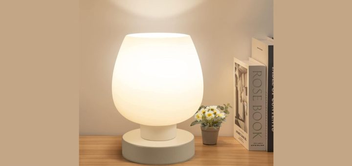 Modern touch bedside table lamp placed on a wooden nightstand in a cozy bedroom.