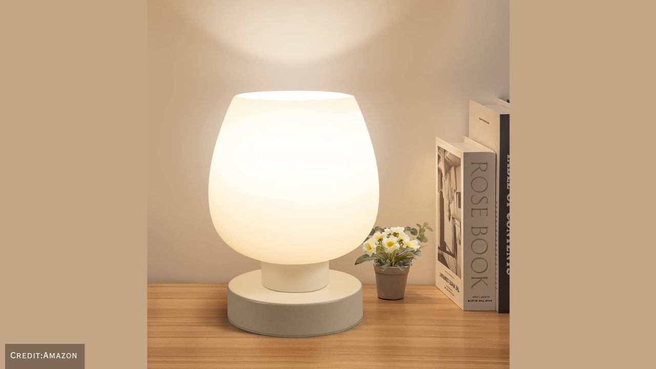 Modern touch bedside table lamp placed on a wooden nightstand in a cozy bedroom.