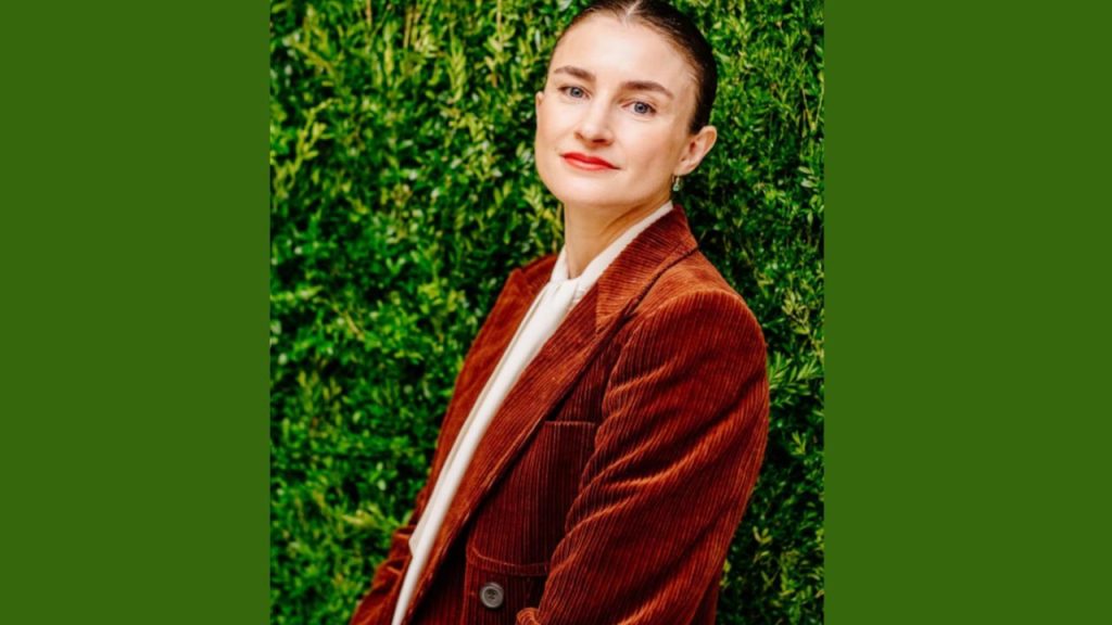 Chloe Malle posing in front of a textured green wall, portraying poise and composure as she embarks on her leadership role at Vogue.