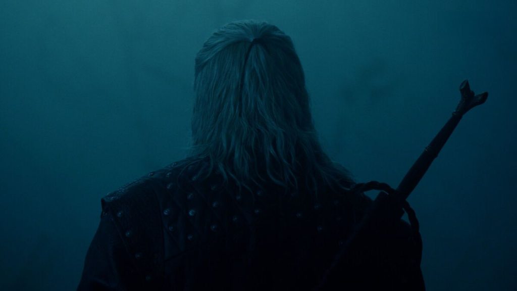 Geralt poised for battle, sword drawn, in a dark forest setting as monster threat looms