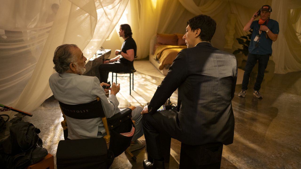 Actor seated on set surrounded by crew in dim lighting during Megalopolis production