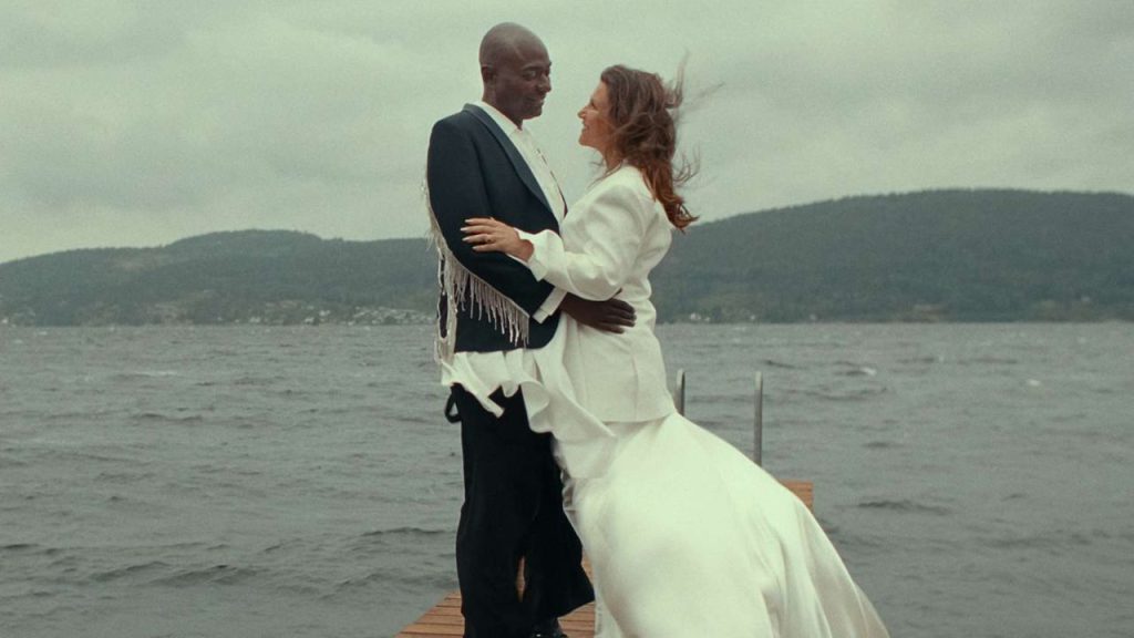 Princess Märtha Louise in a white wedding dress embracing Shaman Durek Verrett on a serene lakeside—scene from Rebel Royals.